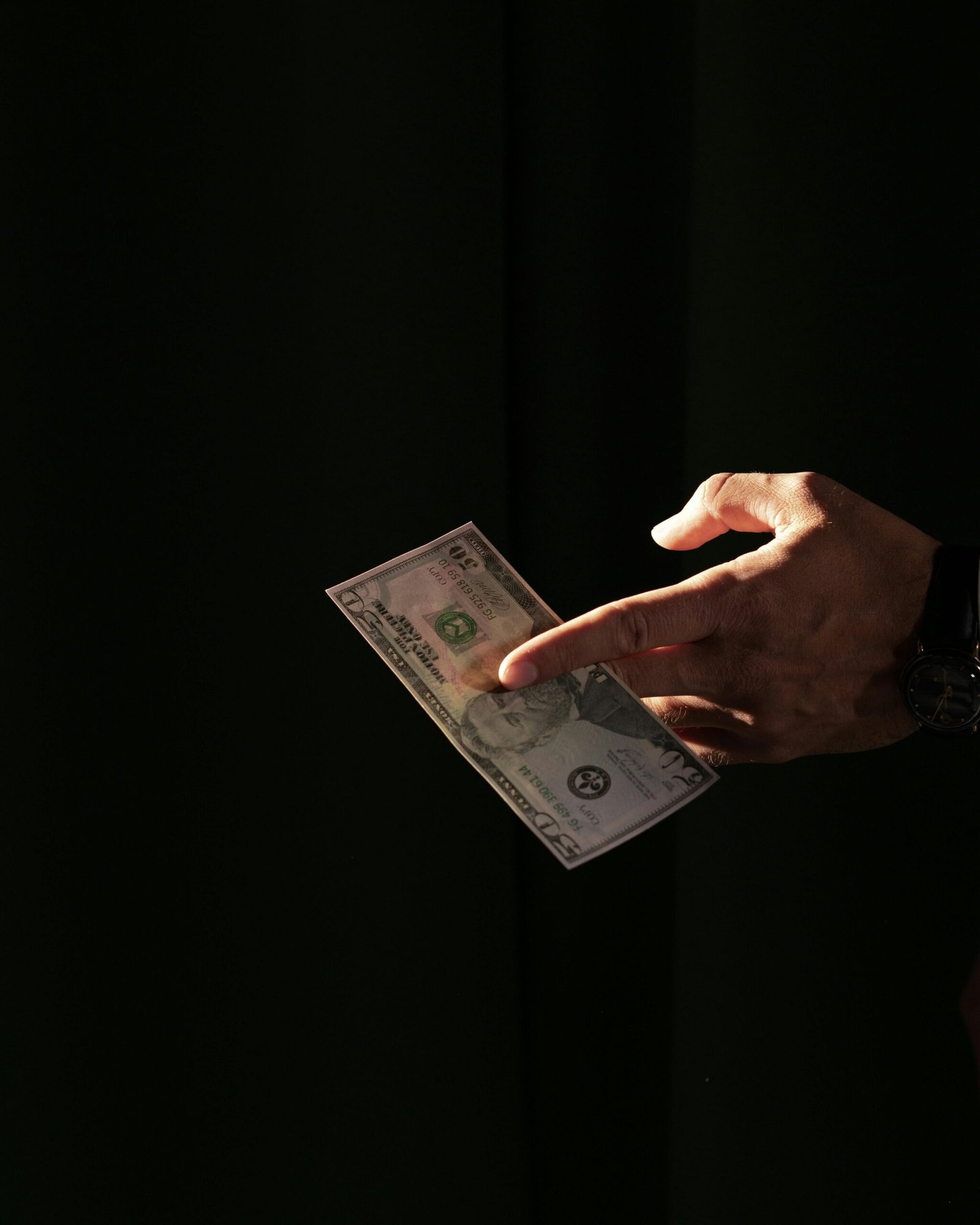 A close-up of a hand holding a US dollar bill against a dark background, highlighting financial themes.